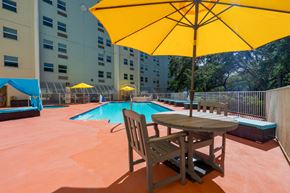 New Port Richey apartment for rent - A yellow umbrella is on a table with a chair in front of a pool.