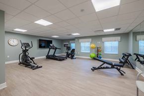 Kalamazoo apartment for rent - A spacious gym with a variety of exercise equipment and a clock on the wall.