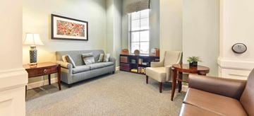 Dublin apartment for rent - A living room with a grey sofa, a brown leather chair, a wooden side table with a lamp, a small table with a plant, and a framed picture on the wall.