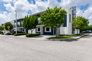 Miami Gardens apartment for rent - A modern building with a white and blue exterior is surrounded by trees and a clear sky.
