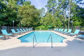 Aiken apartment for rent - A large swimming pool surrounded by trees and lounge chairs.