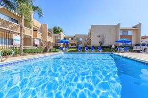 Vista apartment for rent - A large swimming pool in front of a building with a fence and umbrellas.