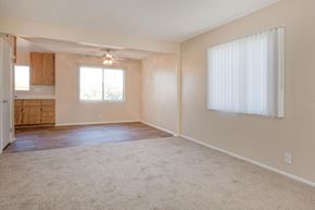 Barstow apartment for rent - A spacious living room with a carpeted floor and a window with white curtains.