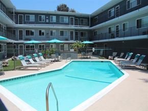 Pico Rivera apartment for rent - A large swimming pool surrounded by lounge chairs and umbrellas in a resort-style apartment complex.