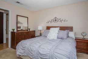 Victorville apartment for rent - A bedroom with a large bed and a dresser with a mirror above it.