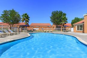 Victorville apartment for rent - A large outdoor swimming pool surrounded by a fence and trees.