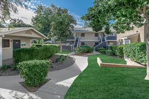 Riverside apartment for rent - a walkway between two apartment buildings with trees and grass