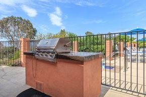 San Diego apartment for rent - A red brick BBQ grill with a black grill grate and a black handle.