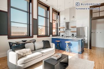 Chicago apartment for rent - A modern living room with a white sofa and a kitchen area in the background.