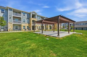 San Antonio apartment for rent - A sunny day at a grassy courtyard with a wooden pavilion and apartment buildings in the background.