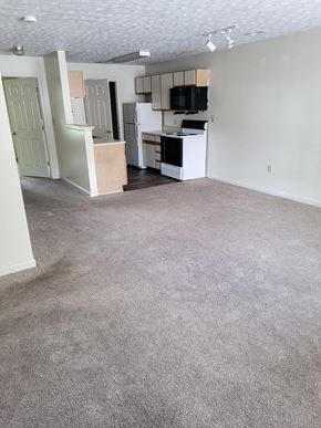 Monticello apartment for rent - Empty living room with a kitchen in the background at Canterbury House apartments in Monticello, Indiana