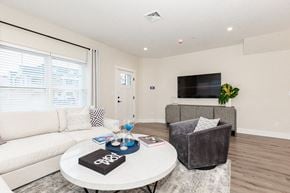 West Babylon apartment for rent - A living room with a white couch, a grey armchair, a coffee table with a black book on it, and a flat screen TV mounted on the wall.