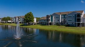 Kissimmee apartment for rent - a fountain is in the middle of a pond in front of an apartment building