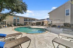 Dallas apartment for rent - A pool surrounded by chairs and umbrellas in front of apartment buildings.