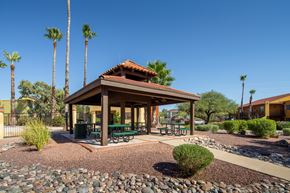 Tucson apartment for rent - A gazebo with a red roof is surrounded by palm trees and a gravel area with a bench.