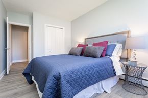 Hamilton apartment for rent - A bedroom with a bed covered in a blue comforter and pillows.