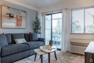 Miami apartment for rent - A living room with a grey couch, a small table with a plant on it, and a painting on the wall.