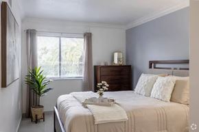 Miami apartment for rent - A bedroom with a large bed and a window with a plant.