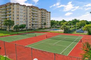 Miami apartment for rent - A tennis court is surrounded by a fence and apartment buildings.