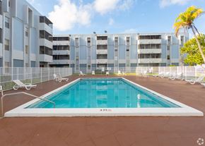 Miami apartment for rent - A large outdoor pool surrounded by a fence and chairs.