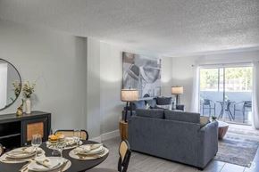 Miami apartment for rent - A modern dining room with a grey couch, a round table set for two, and a view of the balcony.