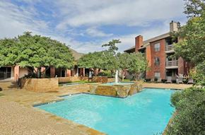 Dallas apartment for rent - A large outdoor swimming pool surrounded by a brick wall and a fountain.
