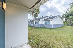 Homestead apartment for rent - A white house with a grey roof is surrounded by a grassy area.