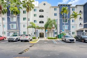 Palm Beach apartment for rent - A parking lot in front of a multi-story building with cars parked.