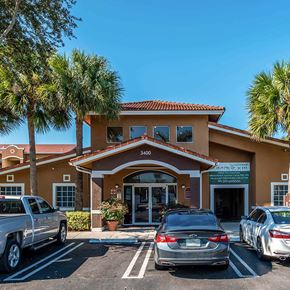 Miami apartment for rent - A building with a brown roof and tan walls with cars parked in front.