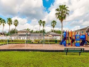 Miami Gardens apartment for rent - A playground with a slide, swings, and a bench is surrounded by palm trees.