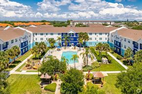 Clearwater apartment for rent - A large swimming pool is surrounded by palm trees and a resort-style building.