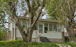 Omaha apartment for rent - A house with a grey facade and a white door is surrounded by trees.