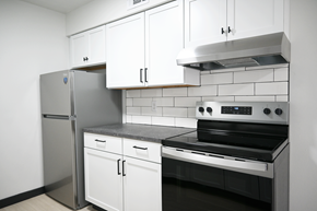 Omaha apartment for rent - A kitchen with a stainless steel refrigerator, white cabinets, and a black stove top oven.