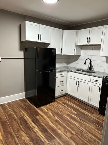 Omaha apartment for rent - A black refrigerator in a kitchen with white cabinets and a wooden floor.