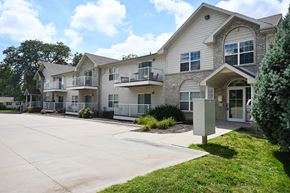 Omaha apartment for rent - Apartment complex with a grey and white building and a sign on the grass.