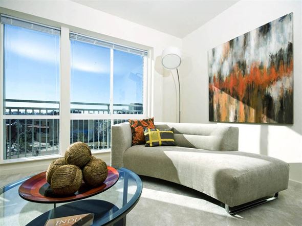 Wheaton apartment for rent - A living room with a grey couch, a glass table, and a large painting on the wall.
