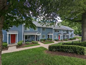 Gaithersburg townhouse for rent - A blue house with a red door is surrounded by greenery.