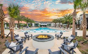 Pensacola apartment for rent - a swimming pool with chairs and a fire pit at sunset