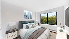 Bronx apartment for rent - A bedroom with a large bed and a window overlooking trees.