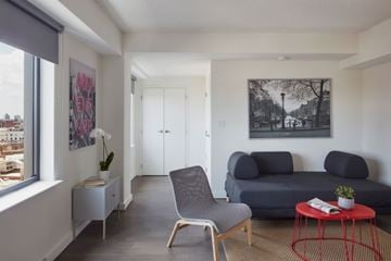 Bronx apartment for rent - A living room with a grey couch, a red table, and a painting on the wall.