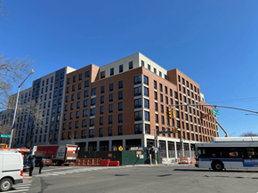 Bronx apartment for rent - A large multi-story building with a red brick facade and a white van and bus in front of it.
