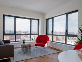 Bronx apartment for rent - A red chair sits in a white room with a view of the city.
