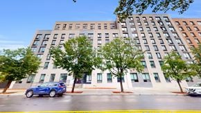 Bronx apartment for rent - A blue car is parked on the street in front of a multi-story building.