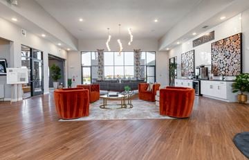 Oklahoma City apartment for rent - A modern living room with a large window, wooden floors, and a mix of furniture including a sofa, armchairs, and a coffee table.