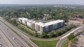 St. Louis Park apartment for rent - A large building with a white roof is surrounded by trees and a highway.