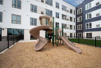 A playground with two slides and a chair in front of an apartment building