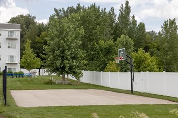 A basketball hoop on the grass in front of a white fence