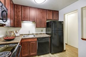 New Hope apartment for rent - a kitchen with black appliances and wooden cabinets at Pheasant Park Apartments, New Hope, MN