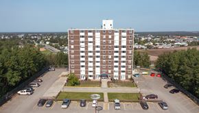 Thompson apartment for rent - A large brown building with a white tower on top is surrounded by a parking lot.