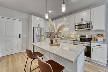 A kitchen with white cabinets and a white island with two chairs.